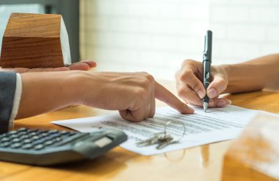 Buyers are signing a home purchase agreement from a broker,model house in broker hand and calculator with a house key on the table.