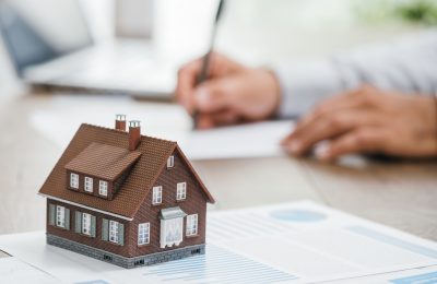 Real estate agent working in his office, he is writing a contract and house model on the foreground: investments, home loan and insurance concept